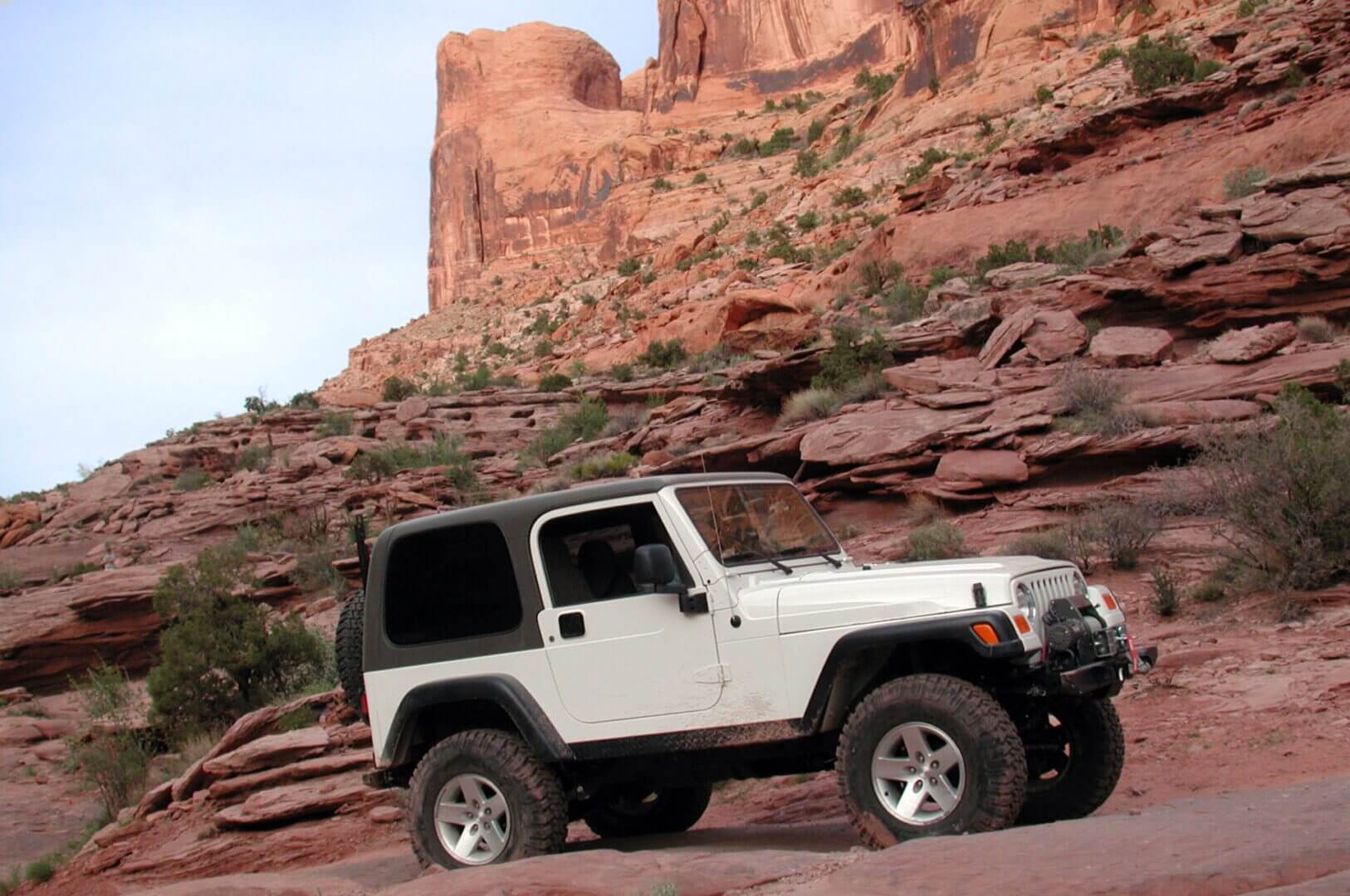 White Jeep traversing red rock terrain.