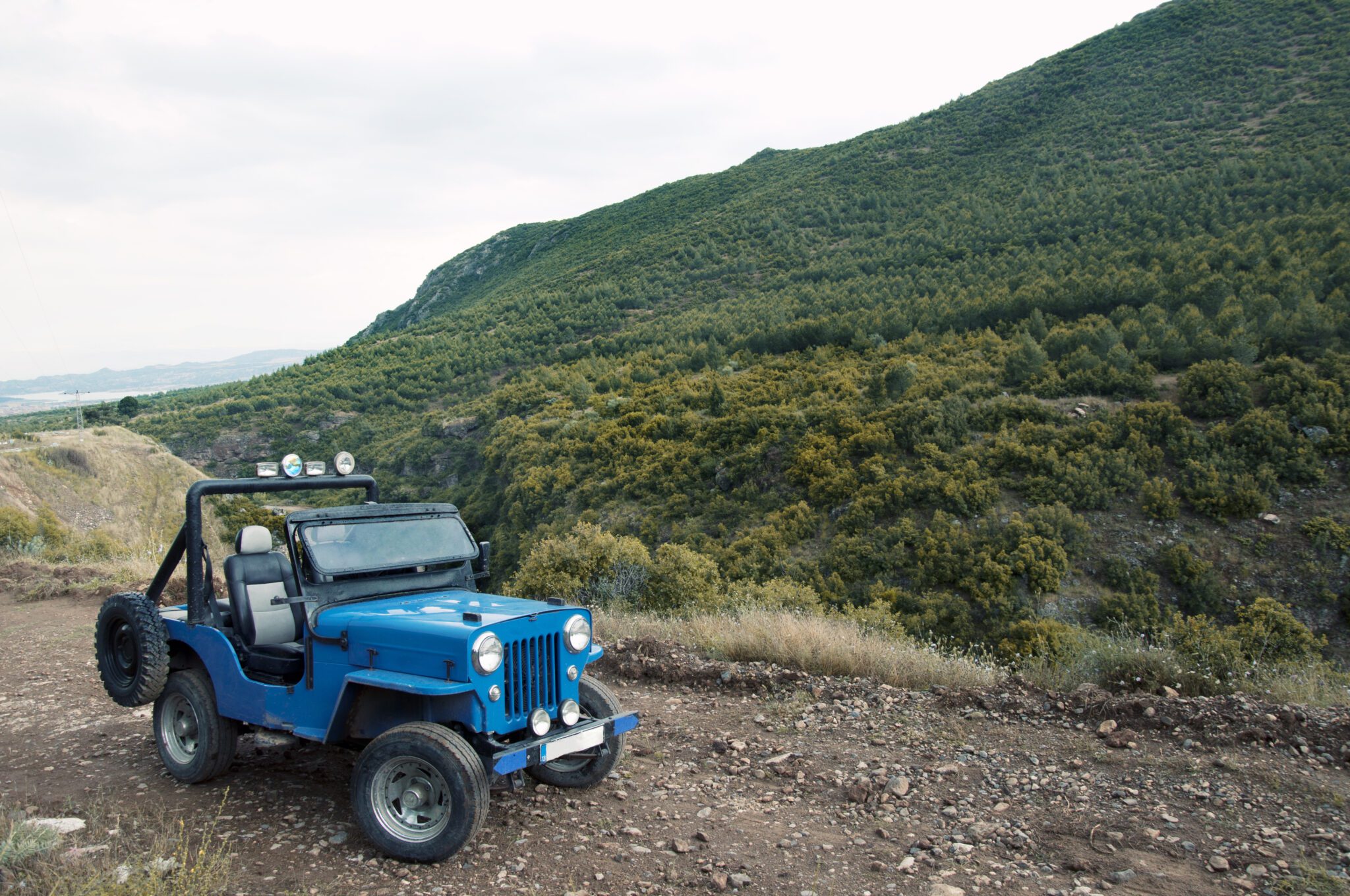 Blue jeep parked on mountainside.